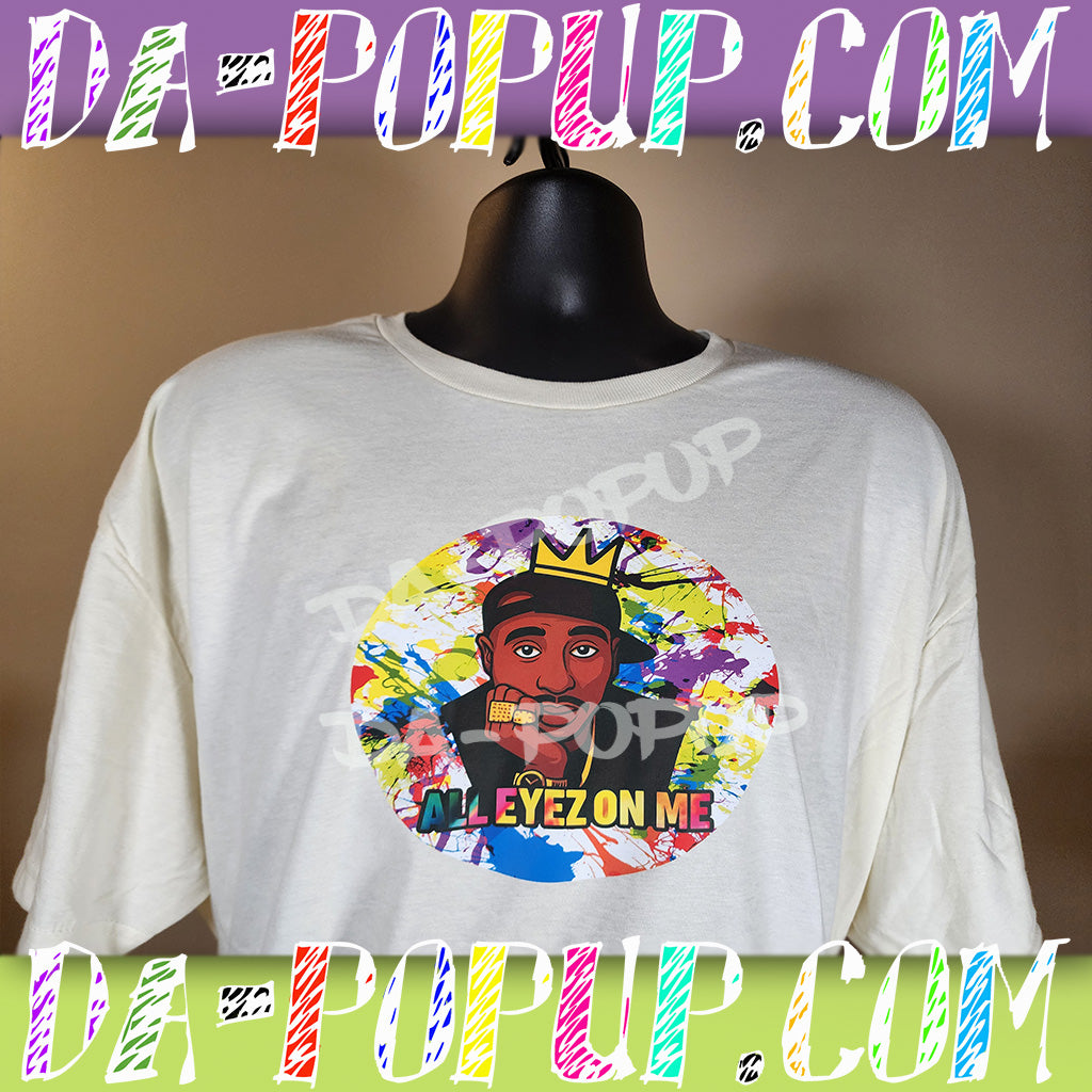 White t-shirt with colorful graffiti splatter design featuring cartoon Tupac with crown and text All Eyez On Me.